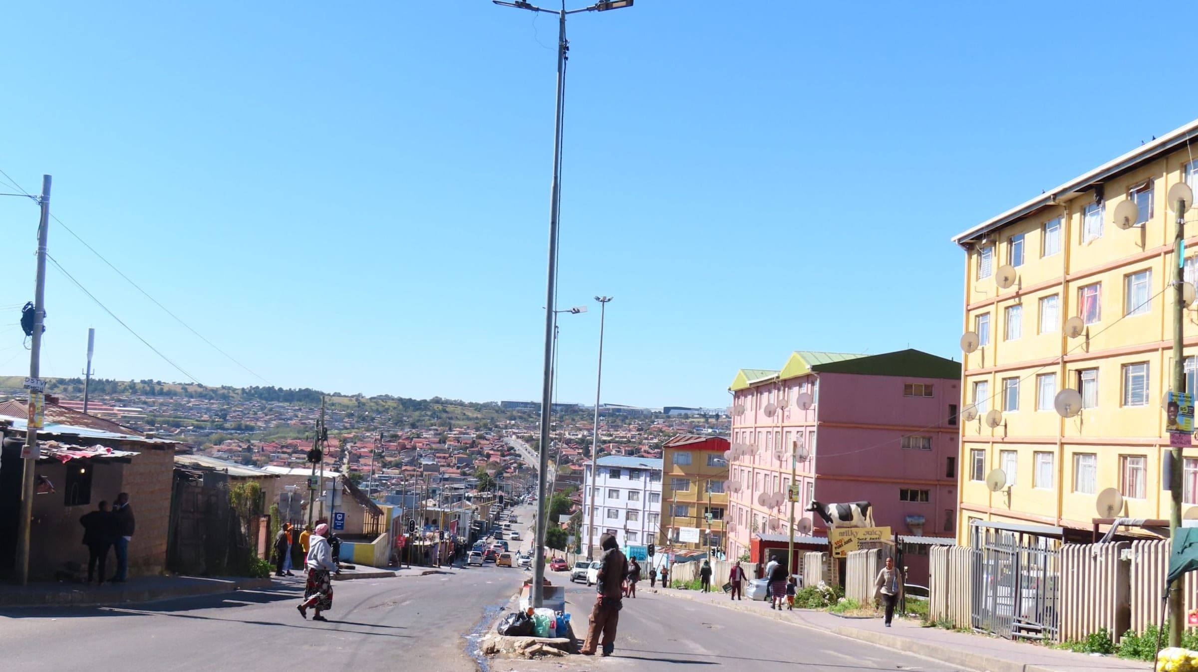 A wide Alexandra street running downhill under a clear blue sky, painted flats on the right and the suburb stretching away to the hills.