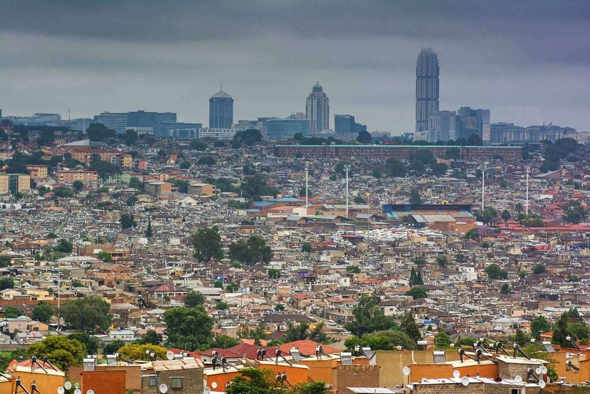 Alexandra's rooftops running to the horizon under heavy cloud, with the towers of the city rising behind them.