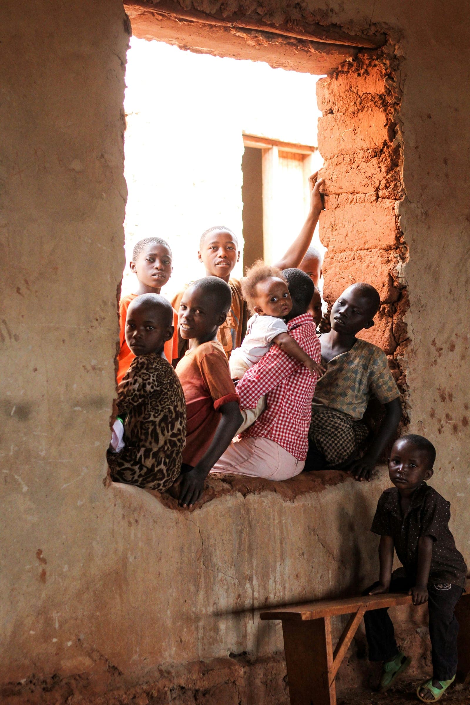 A group of children crowded into the open window of a classroom, looking out together.