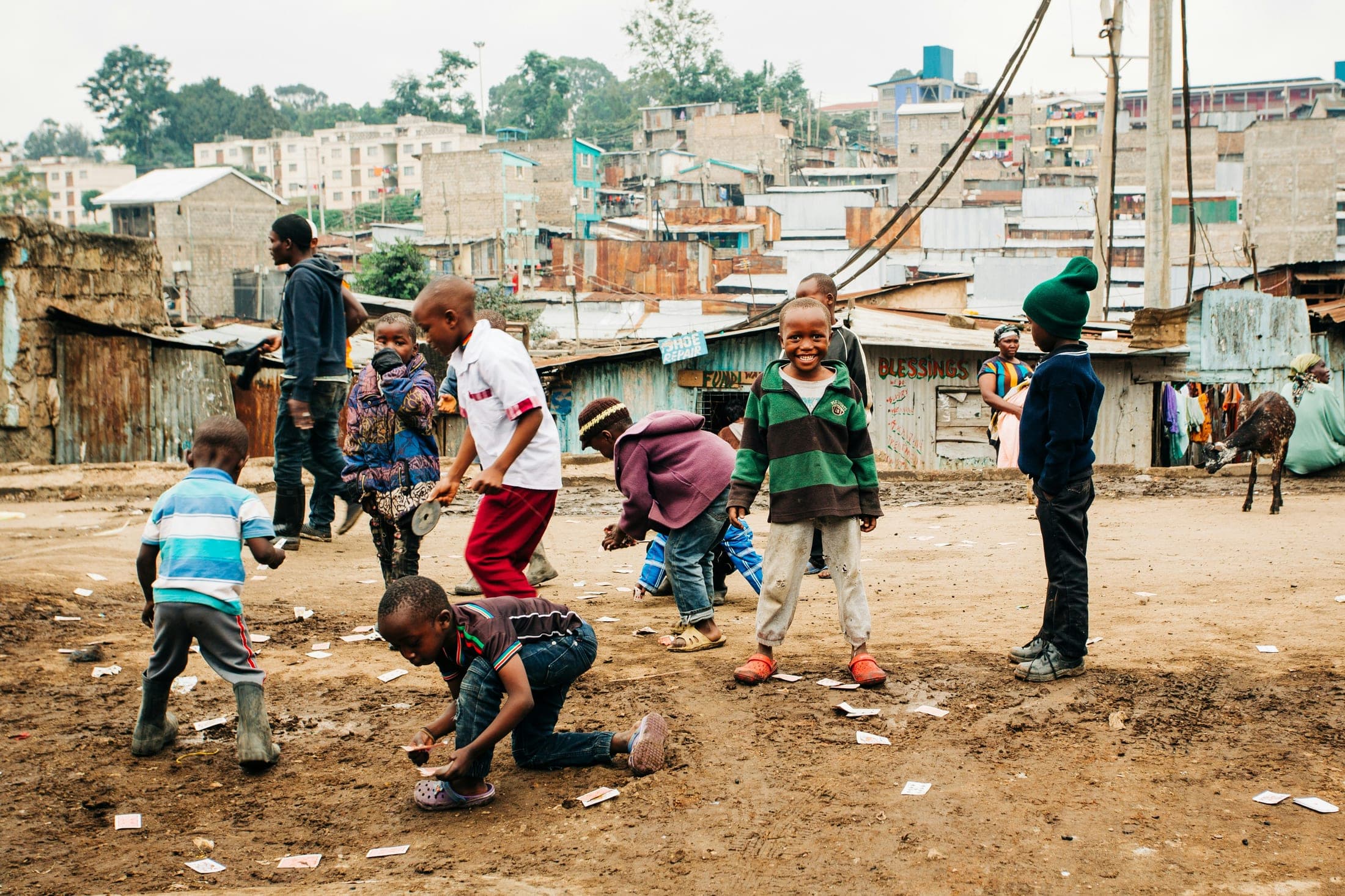 Children playing football together on the open ground between homes, late in the afternoon.