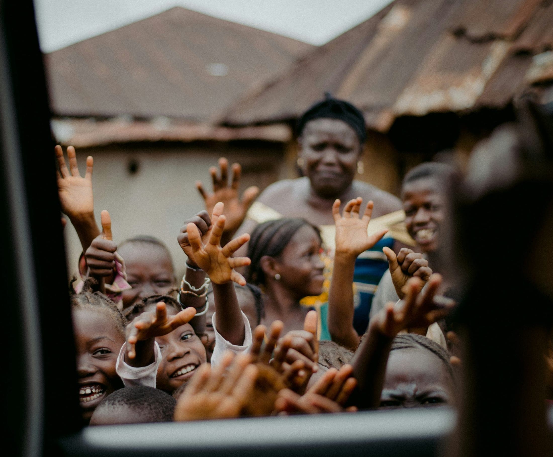 Children and a woman in a community courtyard, hands raised and waving toward the camera.