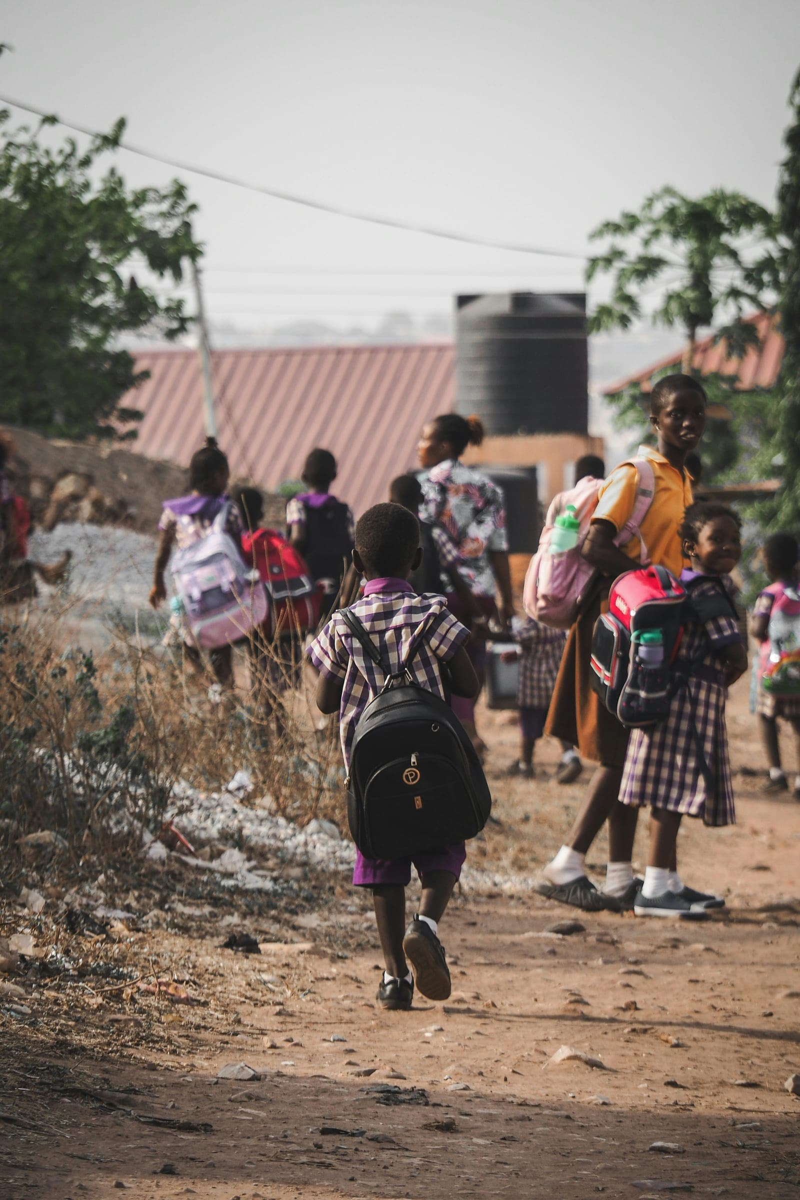 Children walking to school along a dirt path with their bags on their backs.